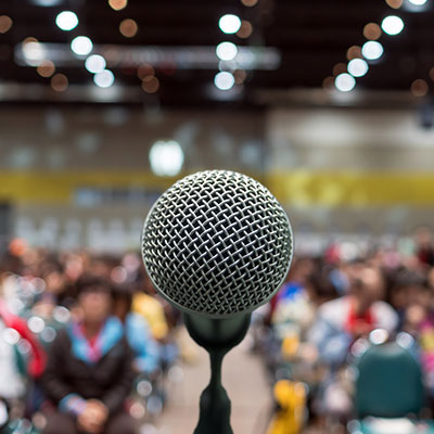 Large microphone with background image of large group of people waiting for the big presentation.
